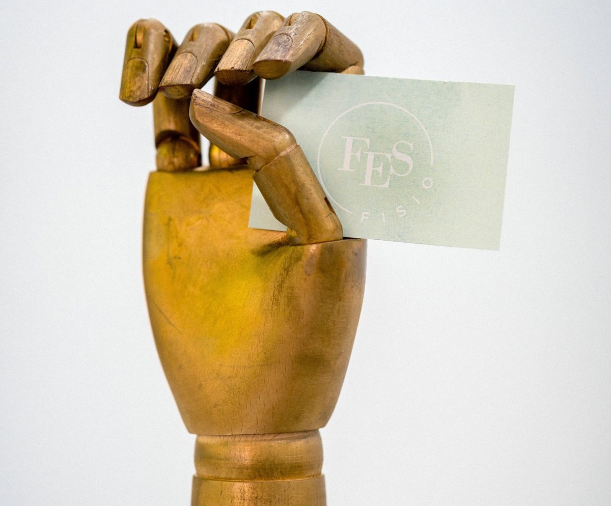 Tarjeta de FES Fisioterapia sostenida por una mano de madera articulada